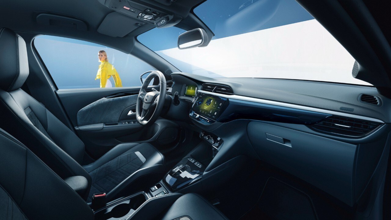 Opel Corsa Electric noir intérieur vue latérale depuis le siège passager avec une femme en arrière-plan en chemise jaune