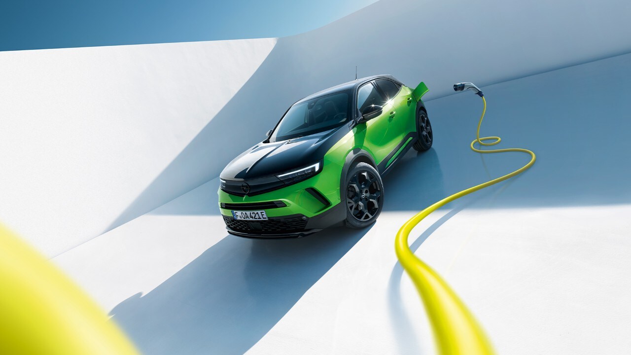 Vue latérale avant d'une Opel Mokka Electric verte avec des jantes noires et un toit avec un câble de recharge EV jaune